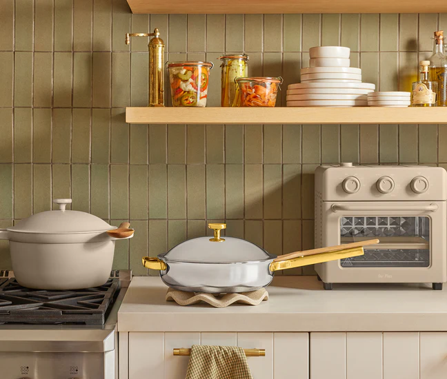 Kitchen scene with pots, pans, and an oven against a tiled wall.